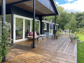 A covered deck with outdoor seating, a potted plant, and a view of a garden.