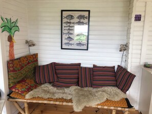 Ett rum med en soffa klädd i vävt tyg, färgglada kuddar, en inramad illustration av en fisk och en vägglampa.