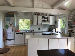 A kitchen with white cabinets, a stove, a sink, and a window with a view of greenery.