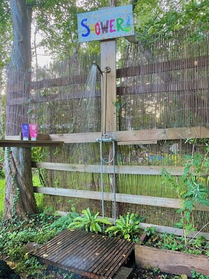 A wooden deck with a bamboo fence, a sign that reads 'SHOWER,' and a small wooden platform with plants.