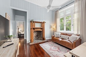 Cozy living room with a fireplace, comfortable sofa, and a view of lush greenery outside.
