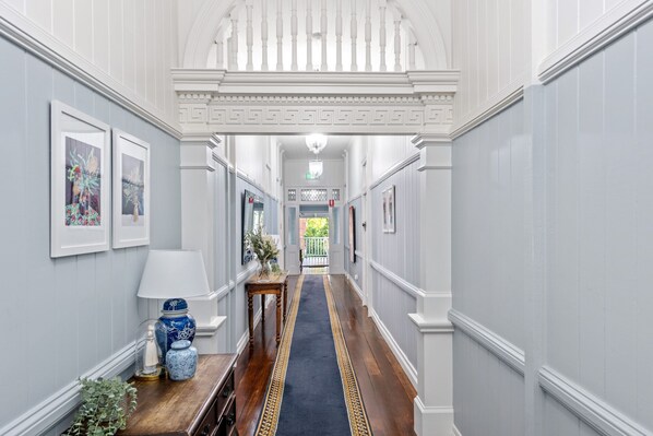 Classic hallway with a central bench, framed pictures, and a carpeted floor leading to a door.