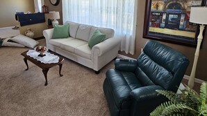 Ein Wohnzimmer mit einem weißen Sofa, einem schwarzen Ledersessel, einem Couchtisch und einem gerahmten Bild an der Wand.