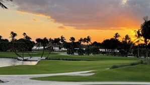 Ein Golfplatz bei Sonnenuntergang mit Sandbunkern und Palmen.
