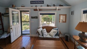 A cozy room with a sloped ceiling, a wooden bench with patterned cushions, a glass door, and a window with a view of trees.