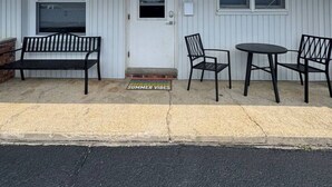 A single-story building with a white exterior, a front door marked with the number 5, a bench, two chairs, and a small table. - Brand New Beach Condo 2BD 1BA w/Parking (Point Pleasant Beach)