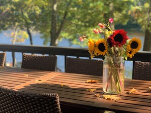 A wooden table with a glass vase containing sunflowers and other flowers, placed on a deck with wicker chairs. - Stunning and Spacious 5 Bedroom LakeHouse with 3 King Beds, 5 Bedrooms, Arcade (Arden, Ontario)