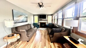 Un salon comprenant un ensemble de canapés, une cheminée, un ventilateur de plafond et de grandes fenêtres.