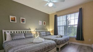 Una cama doble con una colcha estampada y almohadas, una mesita de noche con una lámpara, y una ventana con cortinas.