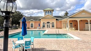 Un área de piscina con sillones de descanso y sombrillas, un edificio con una torre y un cielo despejado.