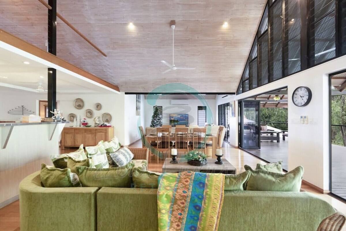 A spacious living area with a green sofa, a dining table, and a kitchen in the background.