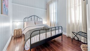 Une chambre à coucher avec un lit en métal, une lampe de chevet, un panier en osier et une fenêtre avec des rideaux.