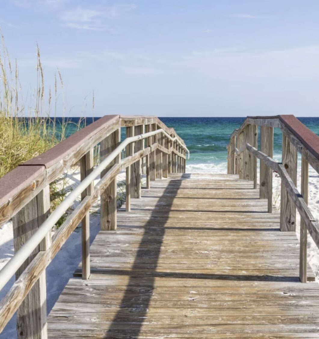 Une promenade en bois menant à la plage, avec des garde-corps de chaque côté.