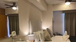 Een hotelkamer met een groot bed, een badkamer met wastafel en spiegel, en een plafondventilator.