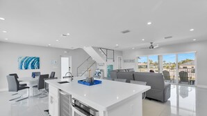 Una cocina moderna con una isla central, comedor con sillas y una escalera que lleva a un balcón con vistas.