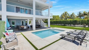 Una casa de dos pisos con piscina, mobiliario exterior y un césped bien cuidado.
