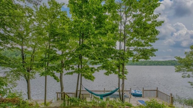 A wooden dock with a hammock, a small boat, and a lake in the background.
