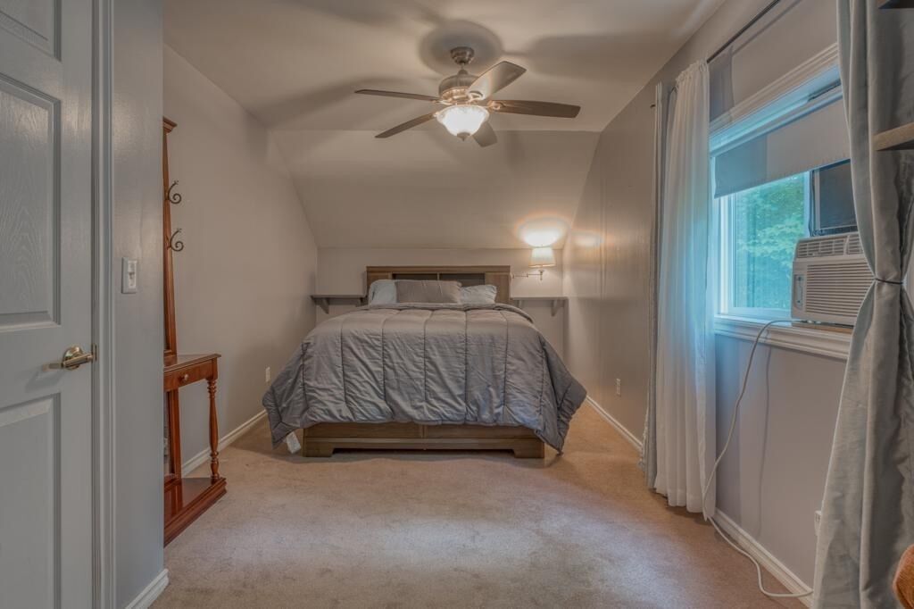 A bedroom with a bed, a ceiling fan, a window with curtains, and a nightstand.