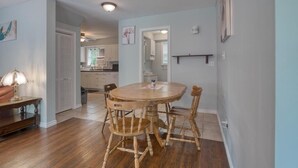 A dining area with a round wooden table and four chairs, a lamp, and a kitchen in the background.