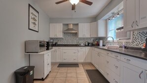 A modern kitchen with white cabinets, a microwave, a toaster, and a ceiling fan.