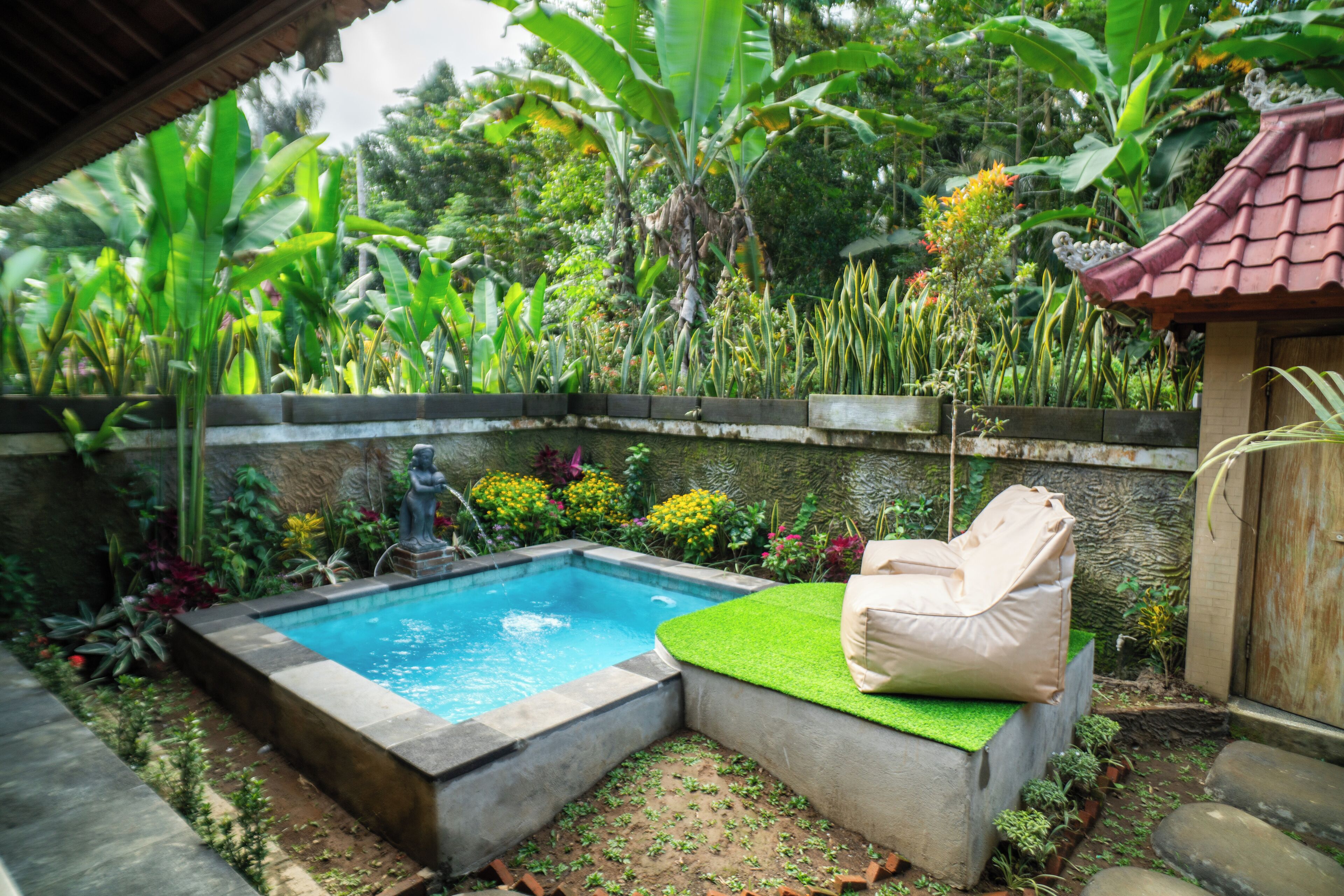 Una piscina con zona de estar integrada, rodeada de exuberante vegetación tropical y un muro de piedra.