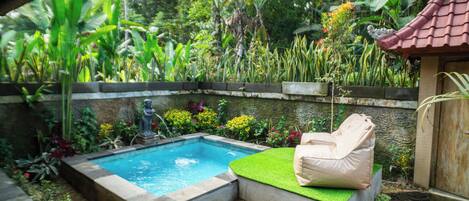 Una piscina con zona de estar integrada, rodeada de exuberante vegetación tropical y un muro de piedra.