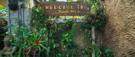A wooden welcome sign surrounded by lush greenery and a stone wall.