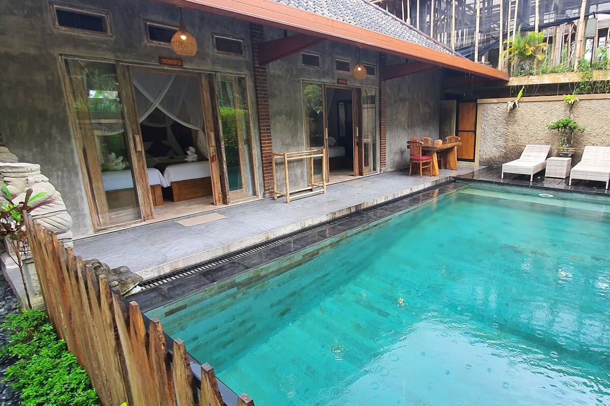 A swimming pool with a wooden deck, lounge chairs, and a stone wall with plants.