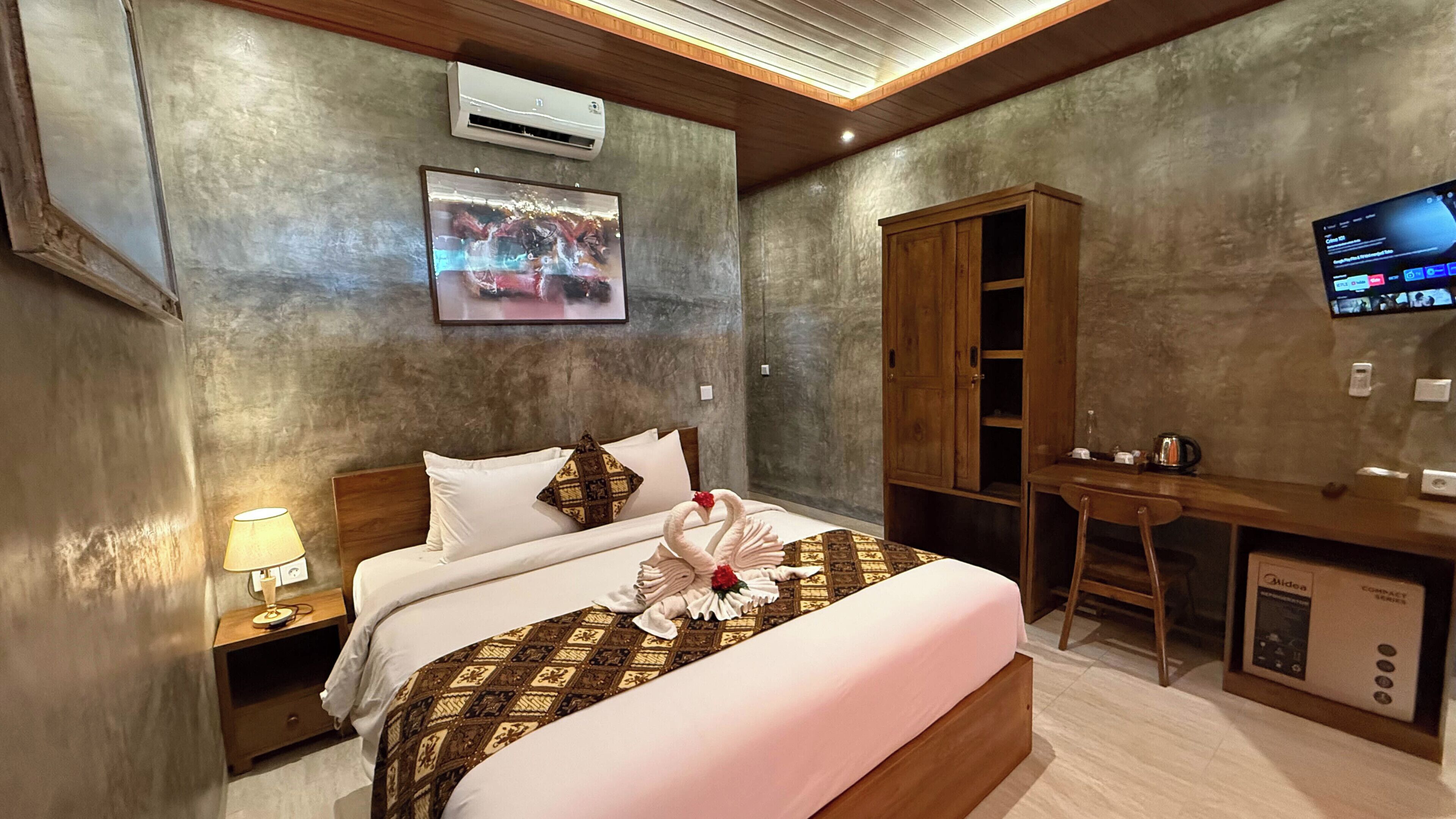 A hotel room with a bed, a desk, a television, and an air conditioning unit.