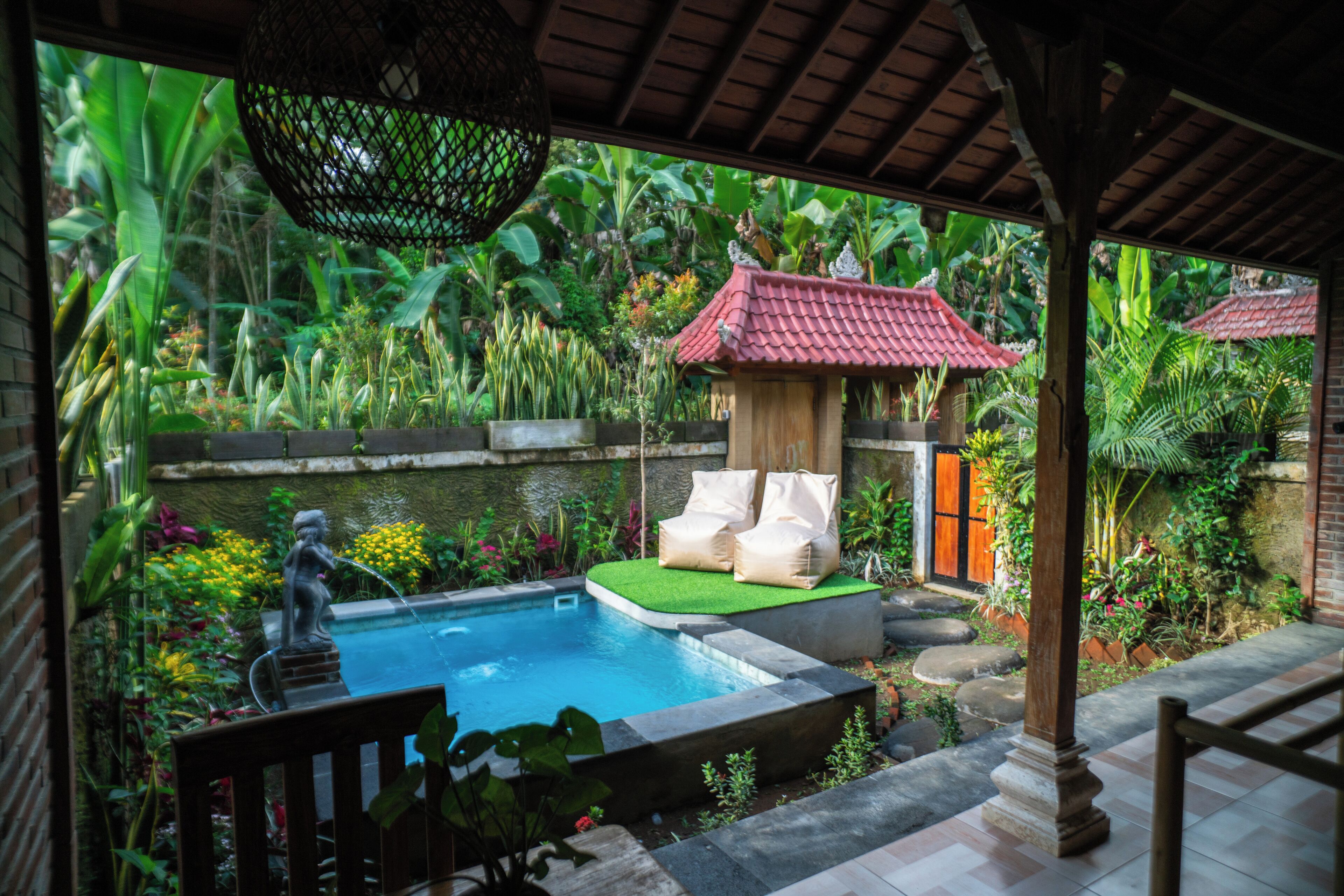 A private pool area with a statue, a small pavilion, and lush tropical plants.