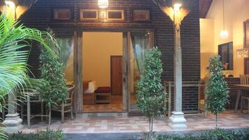 A hotel entrance with a brick facade, wooden doors, and a tiled patio area with small trees and a bench.