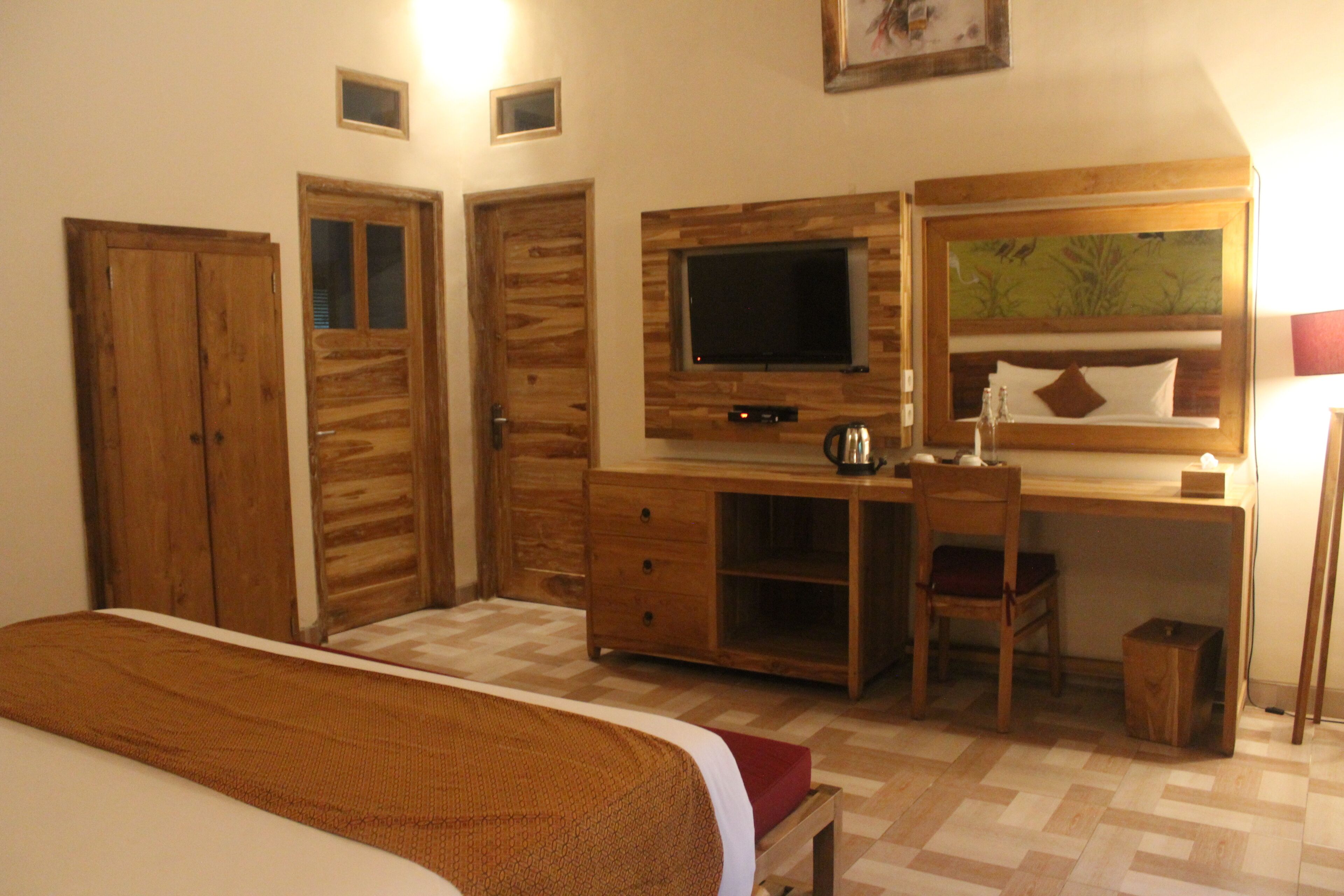 A bedroom with a bed, wooden wardrobe, desk with a chair, television, and a painting on the wall.