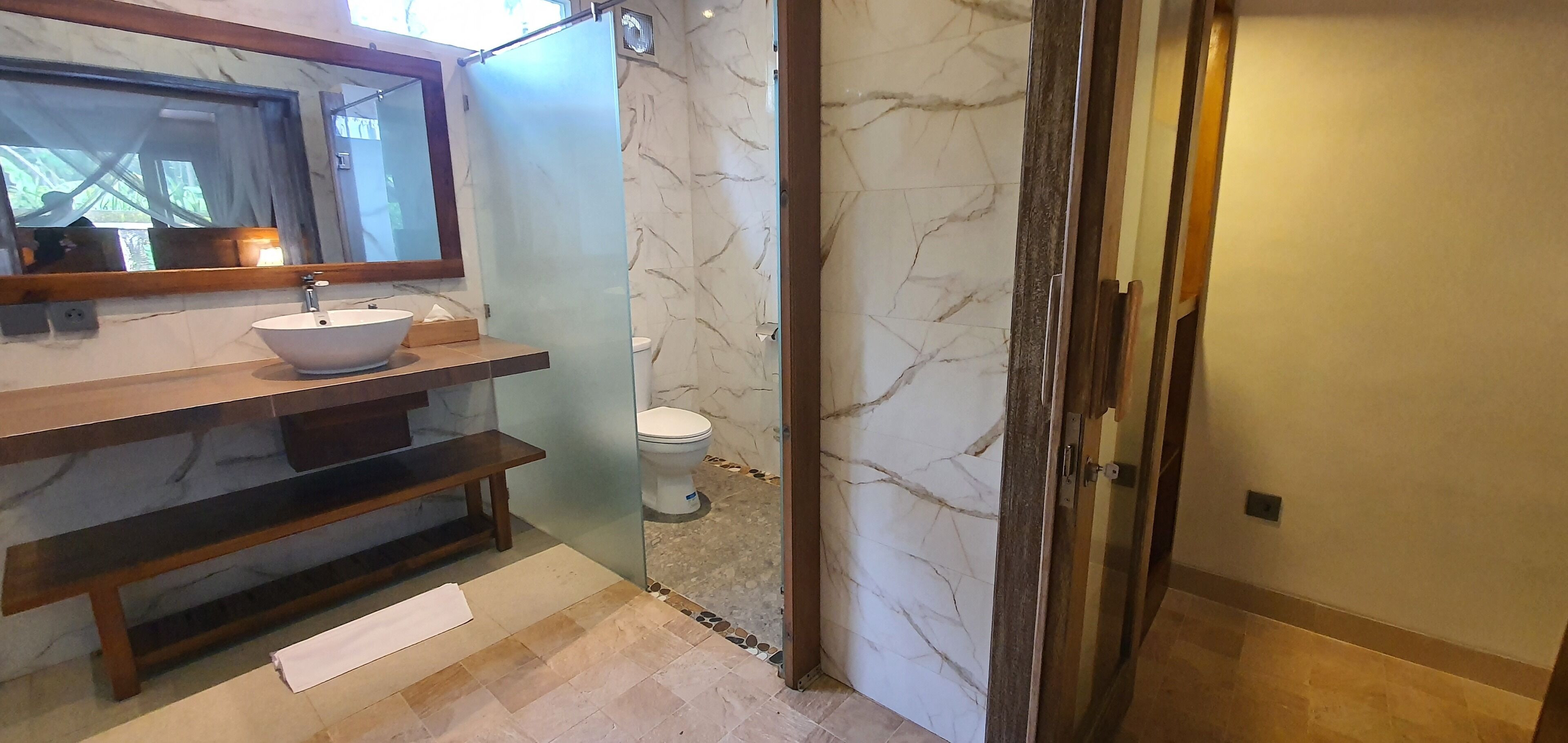 A bathroom with a marble vanity, a sink, a toilet, and a glass shower enclosure.