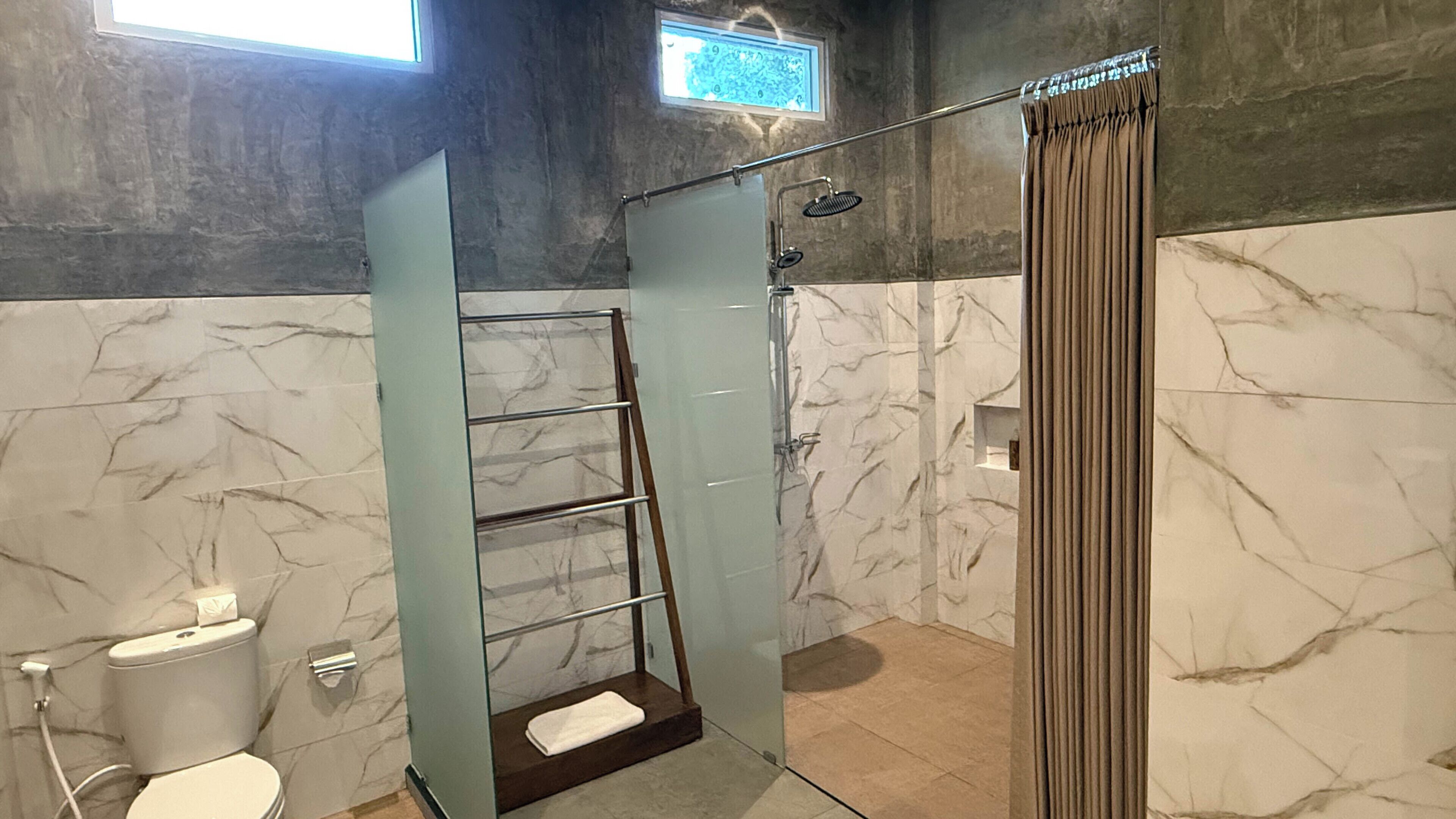 Un baño con cabina de ducha de vidrio, inodoro, perchero y ventana.