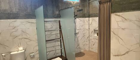 A bathroom with a glass shower enclosure, a toilet, a towel rack, and a window.