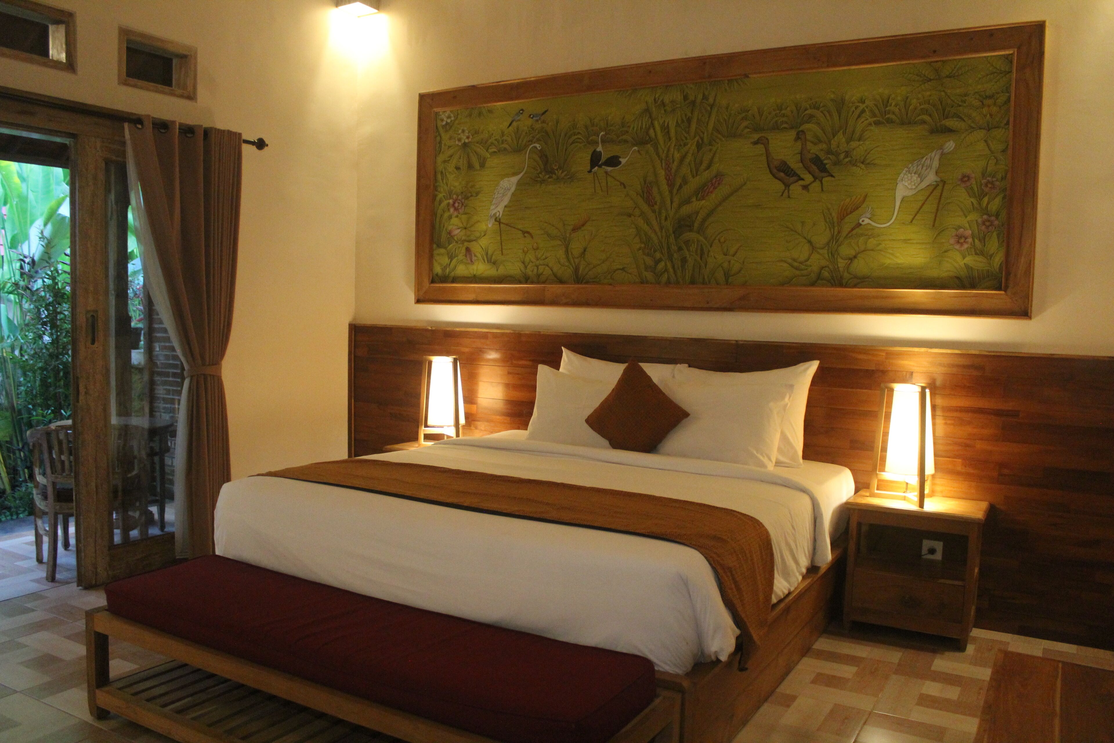 A large bed with a wooden headboard, two bedside lamps, and a large painting above the bed.