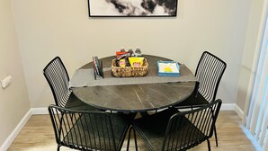 Una mesa redonda de comedor con cuatro sillas negras, un cuadro en la pared y una cesta con aperitivos y bebidas sobre la mesa.