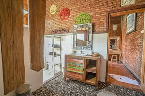 Un baño con tocador de madera, un espejo y un lavabo. Se observan adornos en la pared y una puerta de madera.