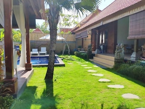 Un jardín cuidado con piscina, escalones de piedra y un área de descanso techada.