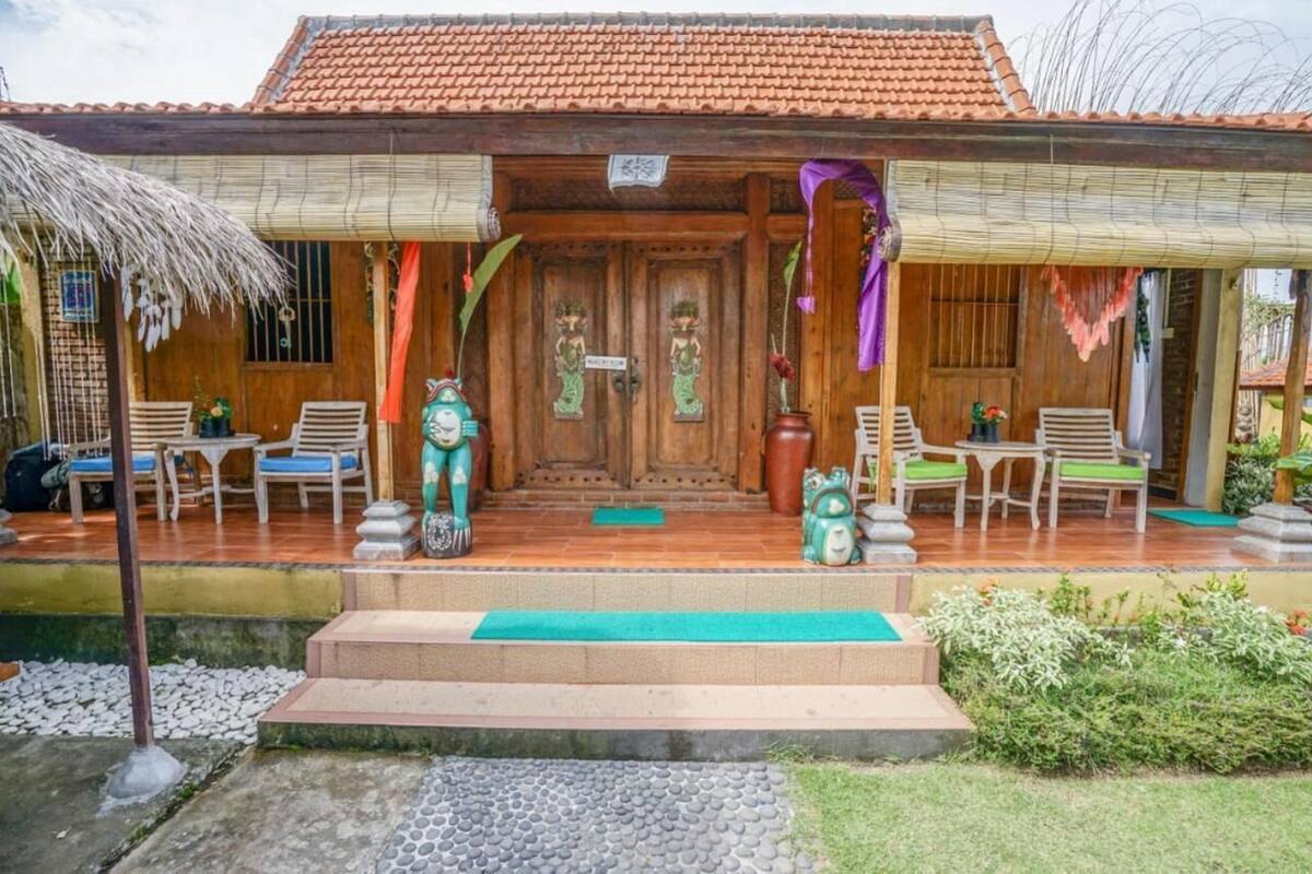 Una casa de madera con techo de tejas, un porche con sillas y un pequeño jardín.