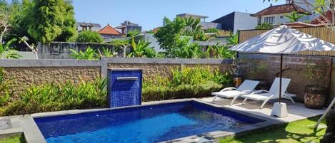 A rectangular swimming pool with a tiled edge, surrounded by a stone wall and lush greenery.