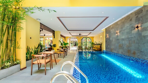 Una piscina interior con agua azul cristalina, rodeada de paredes amarillas y plantas de bambú.