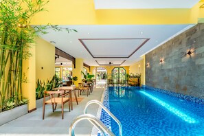 An indoor swimming pool with clear blue water, surrounded by yellow walls and bamboo plants. - Chillax Old Town Villa (Da Nang)
