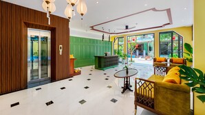 Un vestíbulo espacioso con un mostrador de recepción de madera, una pared revestida de paneles verdes y una pared de acento amarilla. Hay una zona de estar con un sofá amarillo y una pequeña mesa.