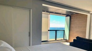 A hotel room with a large bed, a sofa, a balcony with a view, and a sliding door. - Atlântico Vista Mar Deluxe (Fortaleza)