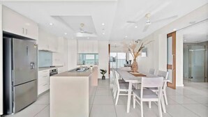 Una cocina moderna con armarios blancos, un refrigerador de acero inoxidable y un comedor con sillas y mesa blancos.