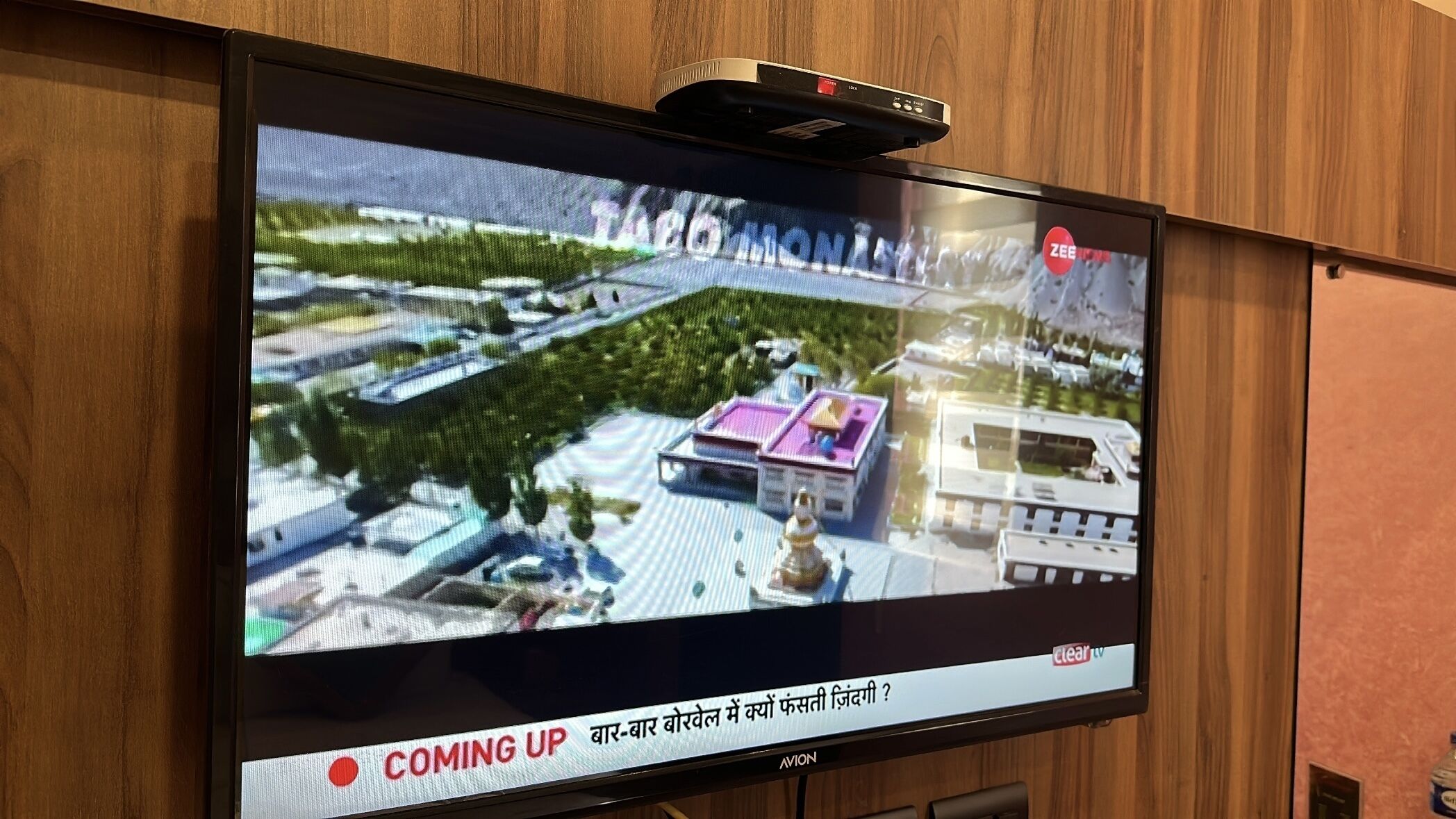 A television screen displaying a 3D model of a modern building with a rooftop garden and a clear sky.