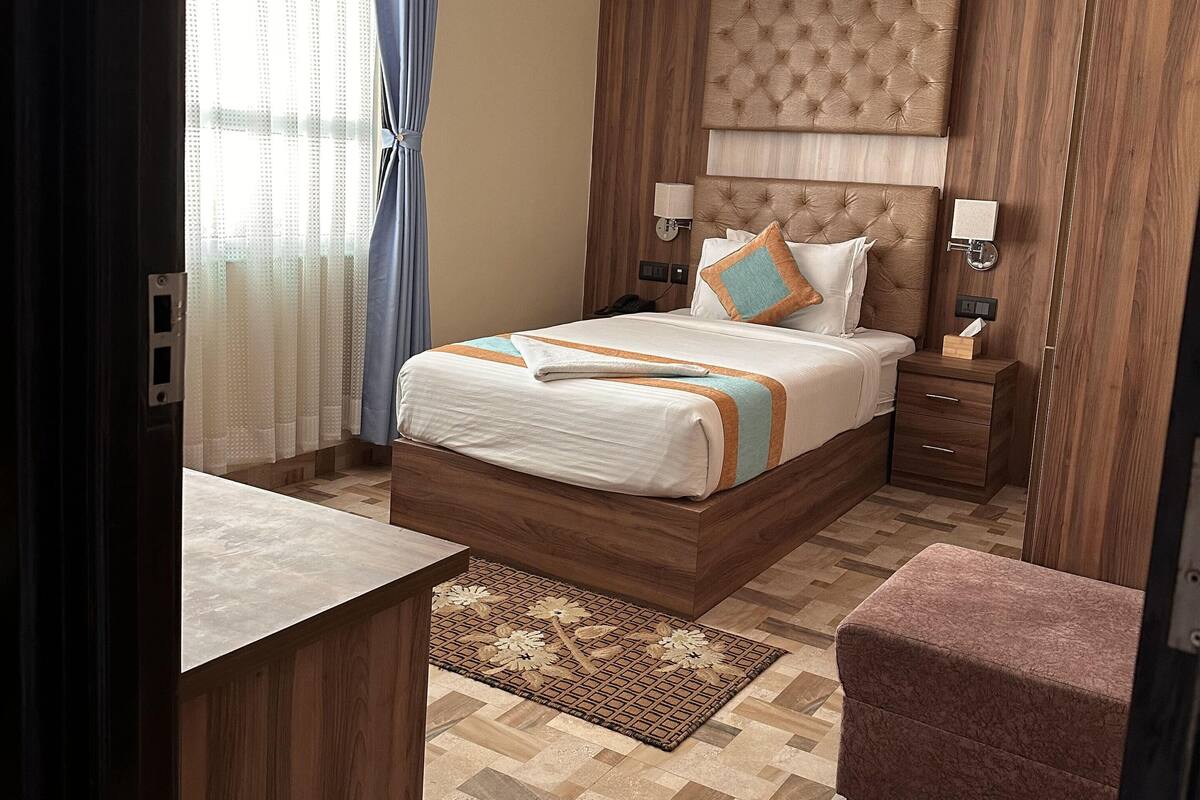 A modern bedroom with a large bed, wooden headboard, bedside tables, and a small seating area.