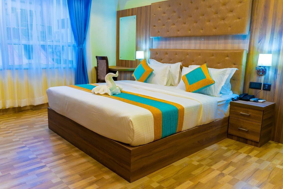 A hotel room with a large bed, wooden headboard, and a nightstand with a phone and remote controls.