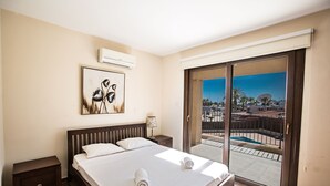 Habitación de hotel con una cama grande, una mesita de noche, aire acondicionado montado en la pared, un cuadro y una puerta corrediza de vidrio que da a un espacio al aire libre.